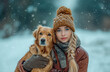 A girl and a dog are sitting on the ground, both wearing hats. The girl smiles and the dog wags its tail, under the snow.