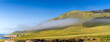 Panorama of rolling hills of grass with clouds, fog