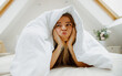 a woman is making a funny face while laying under a blanket on a bed