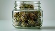 Closeup of a glass jar filled with marijuana buds against a white background