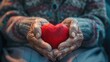 Elderly senior person or grandparent's hands with red heart in support of nursing family caregiver for national hospice palliative care and family caregivers month concept