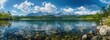 Beautiful panoramic view of a mountain lake in summer with a forest and snowcapped mountains in the background. Beautiful panorama