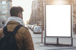 A man in winter clothes walks in the city looking at a billboard mockup