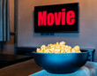 Popcorn in black bowl with television red text MOVIE on display television in living room