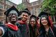 © evgenia_lo - Diverse group of smiling graduates in caps and gowns taking a selfie, with a brick building in the background.
