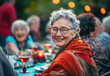A smiling senior woman sitting at a table with friends during a backyard party
