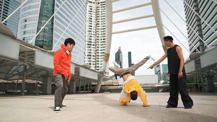 Group of professional happy street dancer cheer up while asian hipster perform b boy dance at urban city surrounded by people with low angle camera. Break dance concept. Outdoor sport 2024. Sprightly.