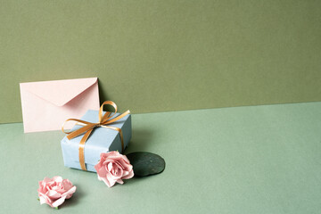 Wall Mural - Blue gift box and envelope card with pink rose on green table. khaki wall background. birthday celebration concept