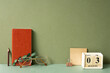 Workspace diary note, calendar, notepad, clip, pencil, eyeglasses, eucalyptus leaf on green desk. khaki wall background