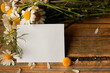 a piece of white paper on a wooden background surrounded by daisy flowers and petals, the concept of romantic mood and love notes, parting, loneliness
