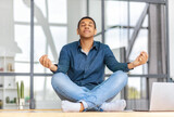 Fototapeta Kuchnia - Calm African American young man sitting on the workplace in the office and meditation taking break avoiding stressful job