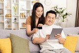 Fototapeta  - Online shopping, couple sitting on sofa with credit card and digital tablet in a cozy living room.