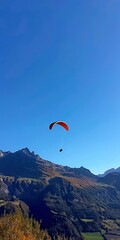 Canvas Print - Paraglider against mountains, close up, from below, clear blue sky 