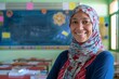 A genial female teacher with a headscarf offering a warm smile in a vibrant classroom environment