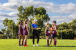 © Austockphoto - female coach holding clipboard addressing schoolchildren in sports uniforms