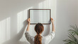 © Oleksiy - Young woman hanging blank frame on light wall at home, back view