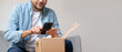 Man in a denim shirt unpacking package and takes a photo of his purchase, internet order. Person sharing feedback with online store using his smartphone.
