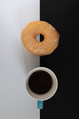 A donut and a cup of coffee are on a black and white background