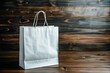 An elegant white paper shopping bag placed upright on a rustic wooden background, showcasing consumerism and retail