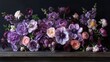   A tight shot of an arrangement of flowers on a table, featuring purple and pink blooms against a black backdrop