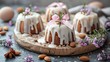   A wooden tray holds bundt cakes, each topped with white icing and garnished with almonds A pink bow adorns the top