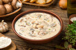 Cream of mushroom soup in a terracotta clay bowl with ingredients on a wooden rustic table.