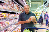 Fototapeta Koty - Elderly man chooses chicken meat in supermarket