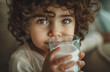 A cute child drinking milk from a glass, with curly hair and brown eyes in a closeup shot of the face.