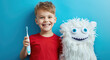 Cute smiling boy holding toothbrush and cute white knitted tooth pattern with eyes isolated on blue background, concept of children's dental health care