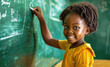 Black girl writing on chalkboard in classroom, smiling and looking at camera
