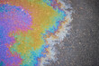 Residues of oil on asphalt left by rain form trails that scatter sunlight, creating a rainbow effect.