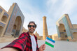 happy tourist traveling in Uzbekistan take selfie photo with uzbekistan flag in in front of the Kalyan minaret and mosque, Bukhara, Uzbekistan.