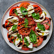 A top-down view of a vibrant Caprese salad arranged on a round plate, with alternating slices of ripe tomatoes, fresh mozzarella cheese, and basil leaves drizzled with balsamic glaze and olive oil.