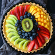 An aerial view of a fruit tart with a buttery pastry crust filled with pastry cream and topped with an assortment of fresh seasonal fruits, such as strawberries, blueberries, kiwi, and mango slices.