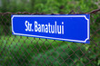 Blue street name plate in Romania, Europe, against green natural background in the summer