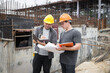 © skarie - Team of construction workers discussing project details with blueprint in construction site.