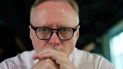 Wall Mural - Focused strict serious face of a senior Caucasian man with fair hair in glasses. Portrait of a tired pensive businessman taking off his glasses thinking hard. Close up.