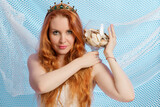 Fototapeta Tulipany - The red-haired mistress of the sea on a blue background with nets holds a glass vase with shells on her shoulder.