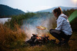 Young calm woman tourist frying vegetables at the beautiful nature landscape while sitting near the tent by the fire. Travel, tourism, camping concept