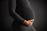 Fototapeta Sawanna - Elegant Pregnant Woman in Striped Dress Holding Her Belly