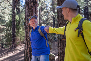 Wall Mural - A happy grandfather and grandson couple hike on outdoor excursion together in the pine forest of Tenerife sharing their passion for nature and healthy lifestyle. The boy helps his tired old grandpa