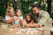 © Zamrznuti tonovi - Fun family making tower of wooden blocks at picnic table in nature.