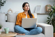 © nenetus - Confident young woman working with her laptop while sitting on a couch at home