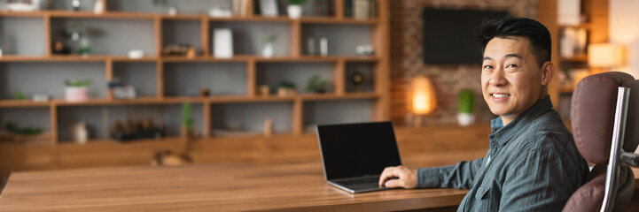 Happy korean man typing on computer with blank screen