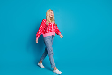 Poster - Full size photo of optimistic person dressed knitwear jumper jeans look at sale walk in empty space isolated on blue color background