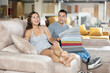 Couple choosing upholstery for lounge furniture in store. Cheerful interested young adult woman and man sitting on couch and looking at samples of colorful fabrics of different qualities and textures