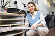 Positive woman employee at copy center putting roll paper on shelves