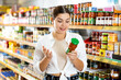 young woman meticulously chooses tomato sauce in supermarket.