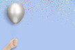 Female hand holds silver balloon on blue background with confetti. Empty space for text