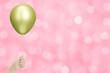 Сhild's hand holding the yellow or golden balloon on blurred pink background. Empty space for text